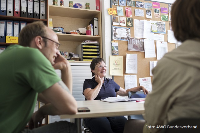 Eine Frau im Beratungsraum erklärt einem Mann und einer Frau etwas