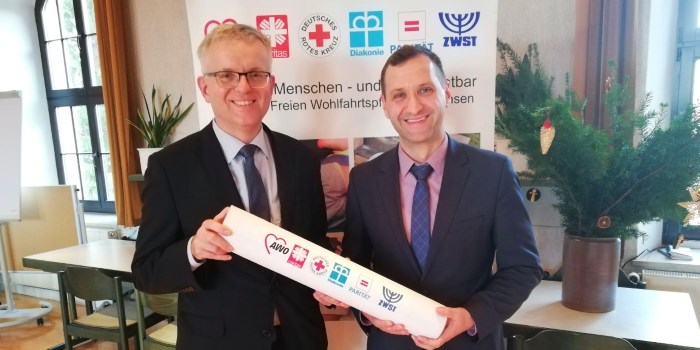 Matthias Mitzscherlich, Caritas Dresden-Meißen, übergibt den Liga-Vorsitz mit einem symbolischen Staffelstab an Michael Richter vom Paritätischen Sachsen.